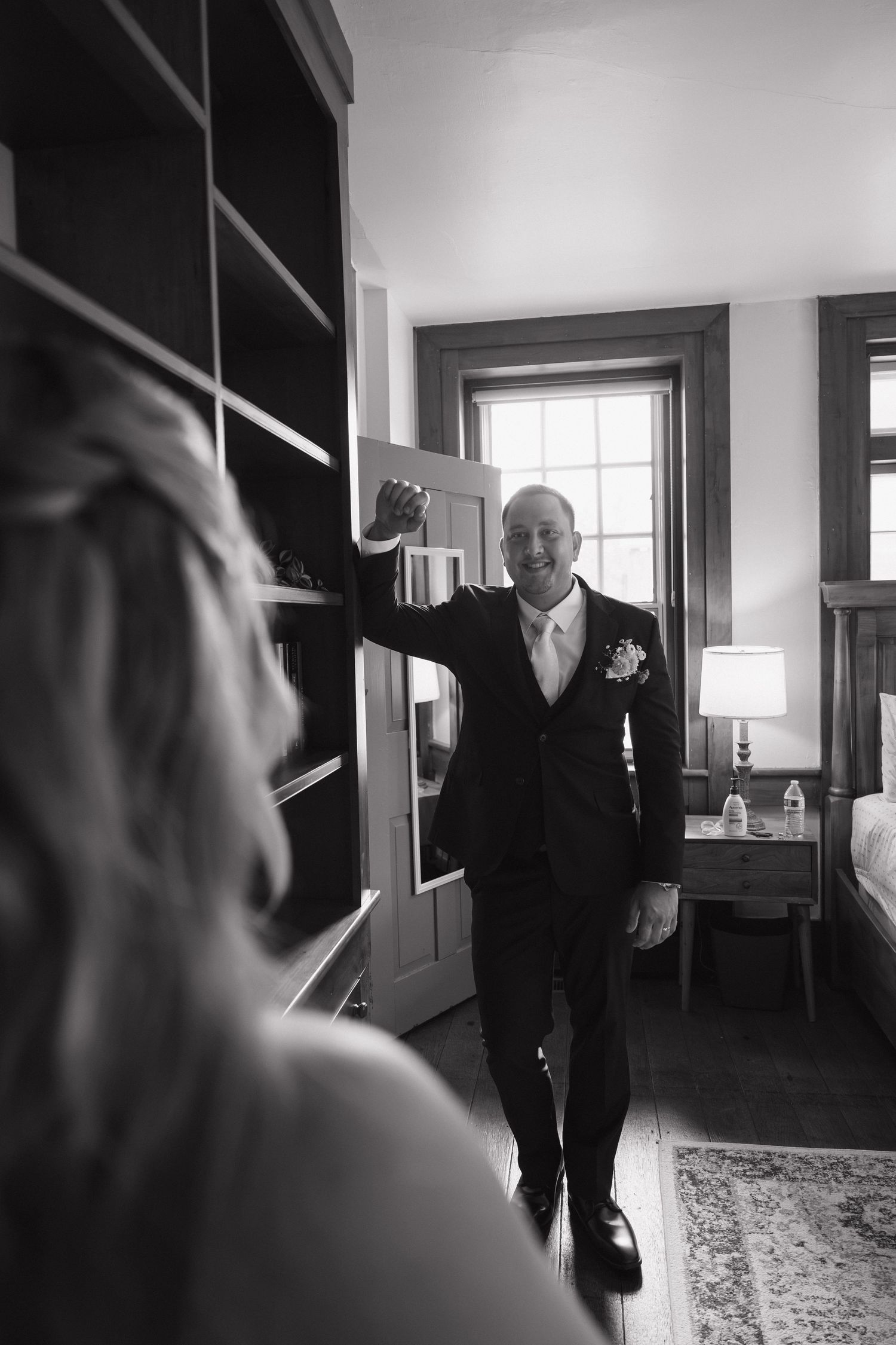 Black and white photo of a smiling groom in a suit with boutonniere seeing his bride for the first time on wedding day.