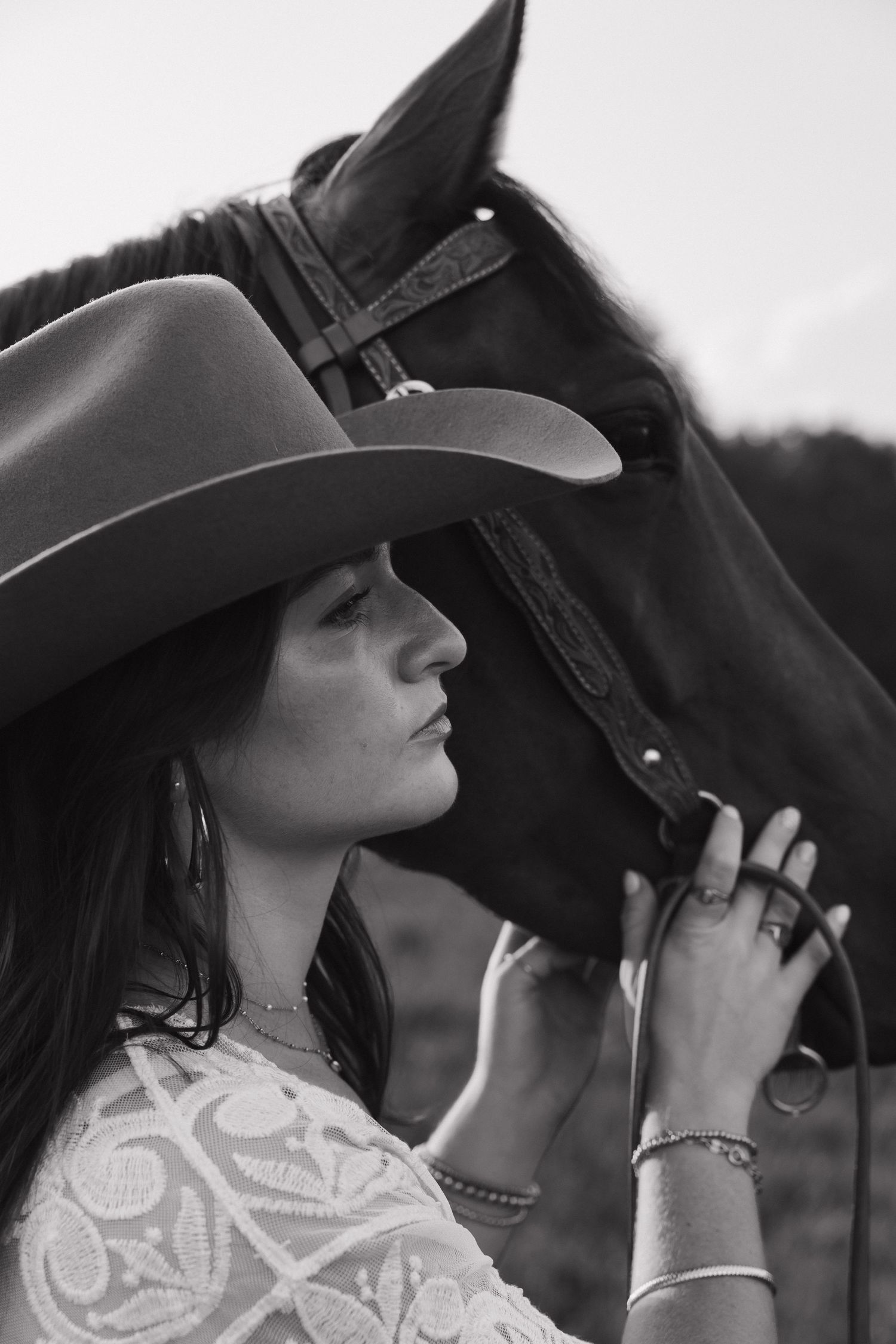 Black and white photo of a woman in a cowboy hat holding the reins of a dark horse outdoors.
