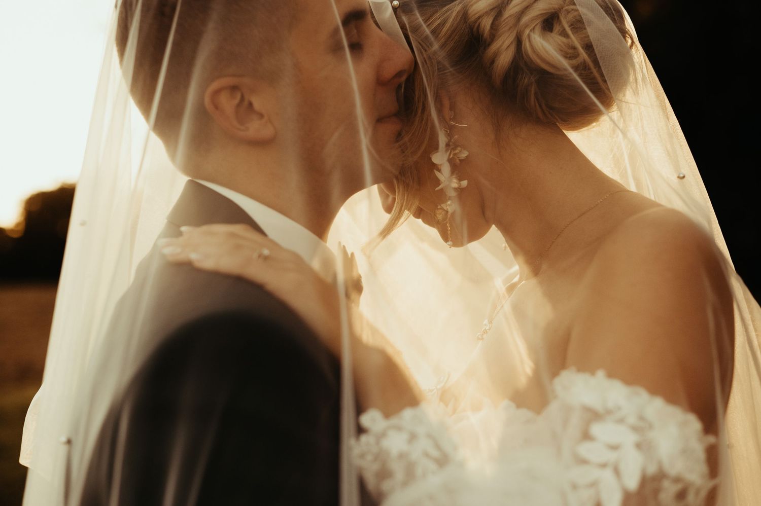 Portrait intimiste de couple de jeunes mariés, sous un voile au coucher de soleil