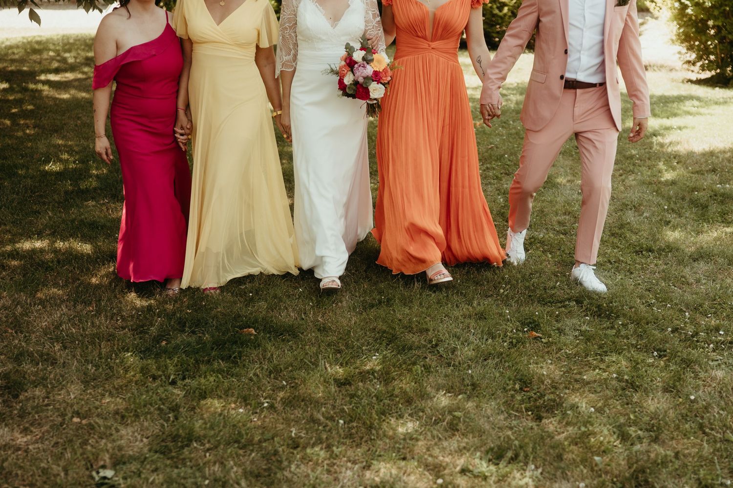 Team d'honneur avec la mariée, détail de leurs tenues colorées pendant qu'ils marchent sur une verte pelouse en Aveyron