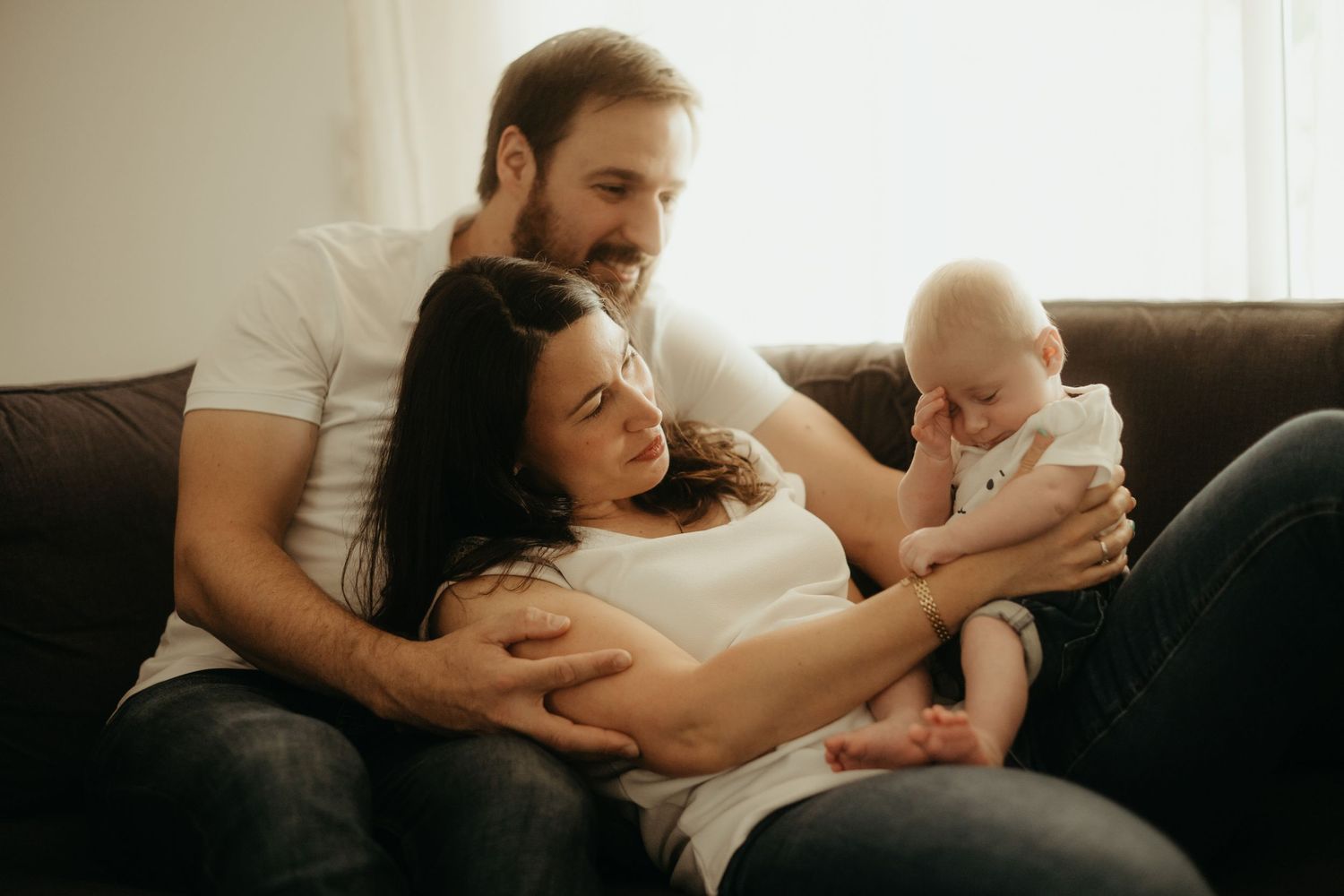 Séance bébé, les parents regarde le bébé fatigué sur le canapé, avec une lumière douce à Toulouse