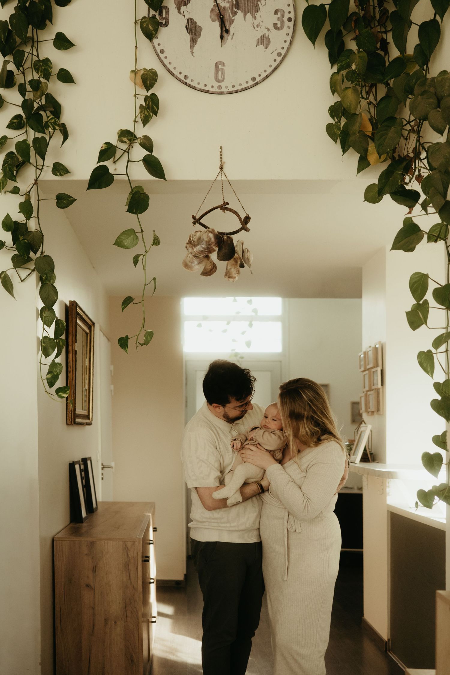 Un couple partage un moment intime en séance nouveau né lifestyle, dans une pièce blanche lumineuse décorée de plantes suspendues à Albi