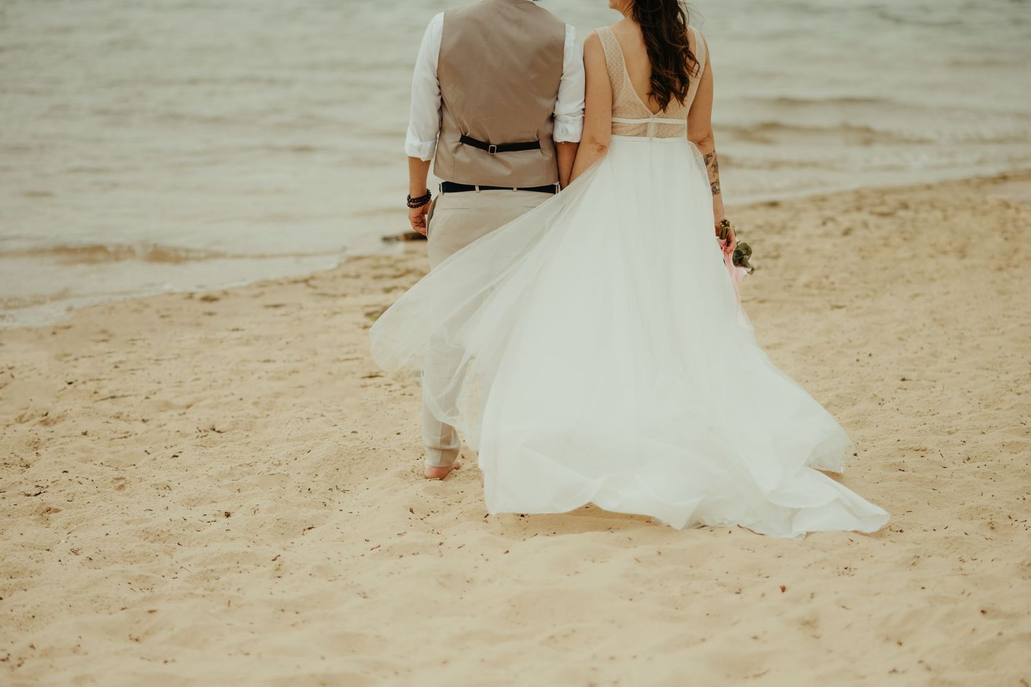 Couple de mariés de dos, la robe au vent, sur la plage du lac d'Hossegor