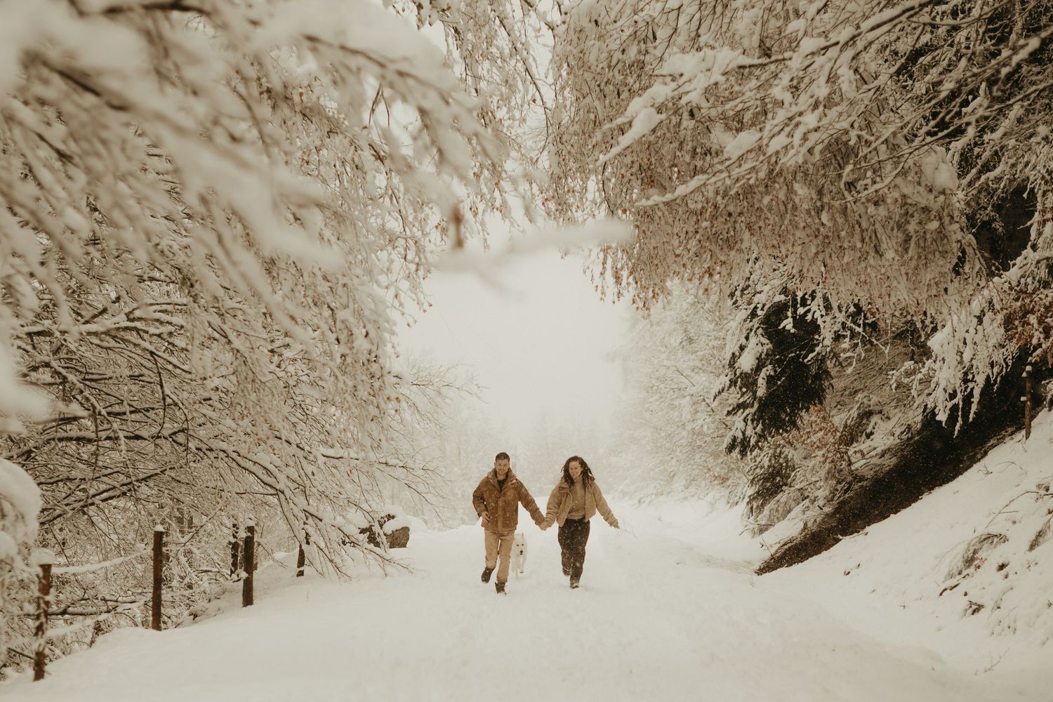Séance photo de couple, qui court main dans la main dans un paysage de neige à Ax les Thermes, avec leur chien