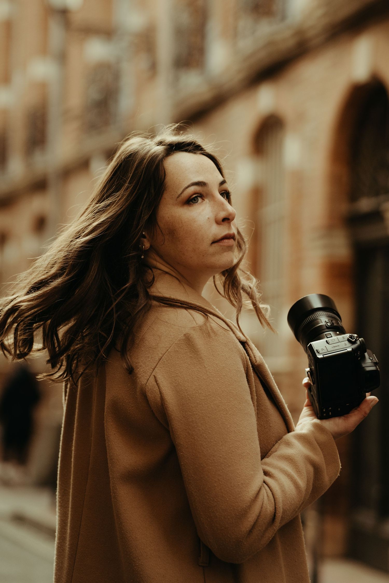 Photographe, tenant son appareil photo Nikon, les cheveux au vent dans les rues de Toulouse