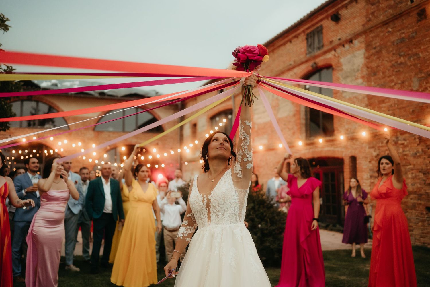 Mariée tenant son bouquet pendant la ronde des rubans, robes et rubans colorés à la tombé de la nuit à Montauban