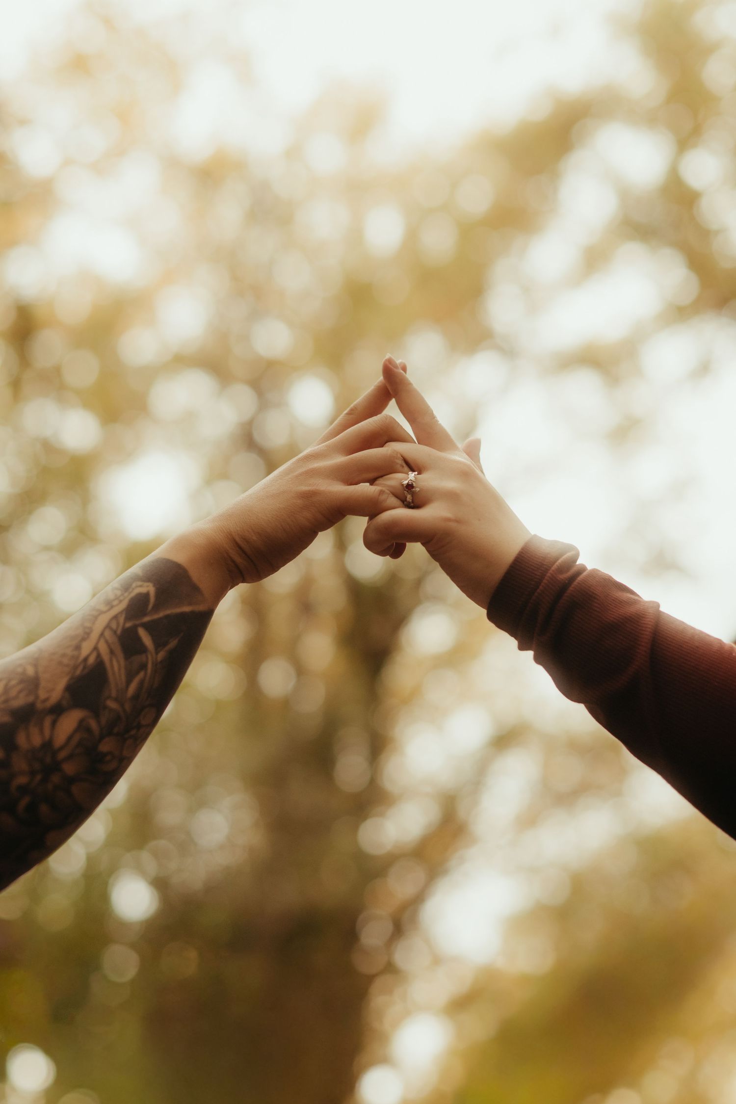 Séance couple, détail de mains d'amoureux avec un bras tatoué en automne dans une forêt à Buzet sur Tarn