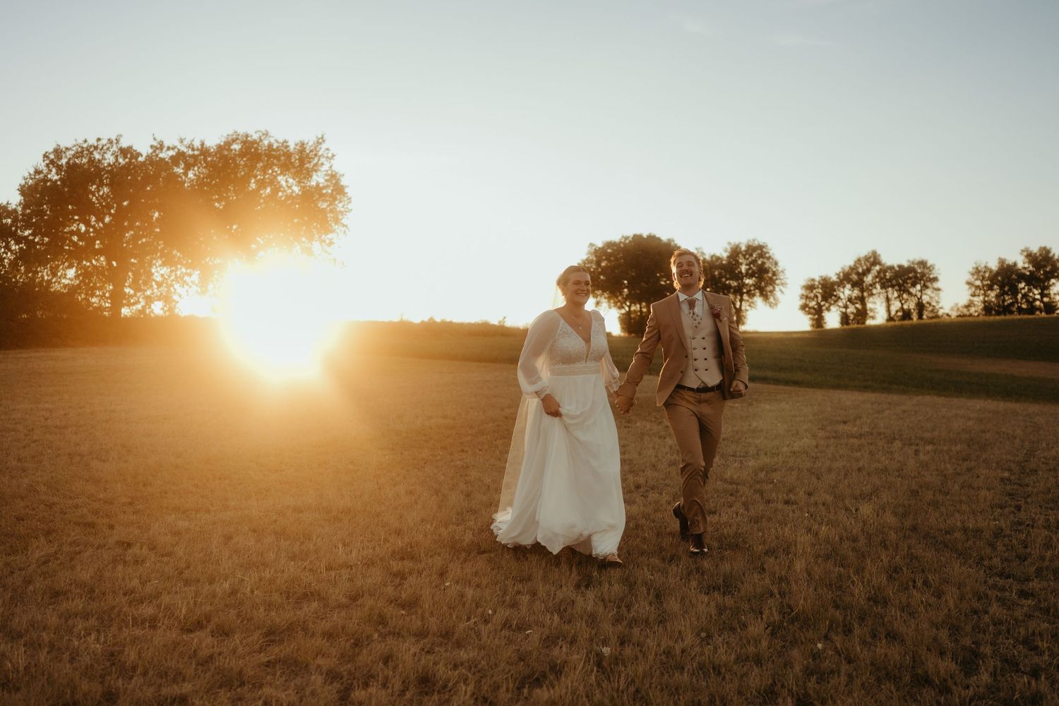 Séance photo de couple, les mariés courent main dans la main au coucher du soleil dans un champ proche de Toulouse