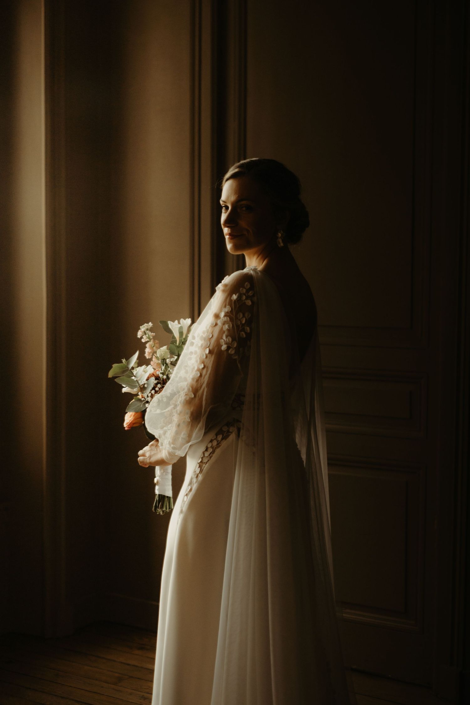 Mariée avec un léger sourire, avant la cérémonie, en clair obscur, dans un château en Charente