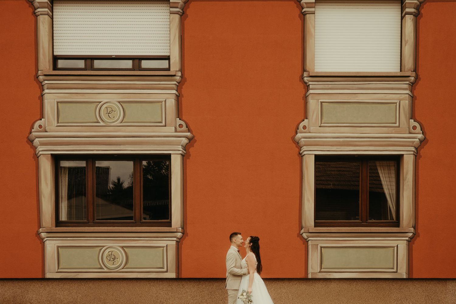 Mariés se regardant, devant une façade de maison orange typique du Bas-Rhin, après leur mariage civil près de Strasbourg