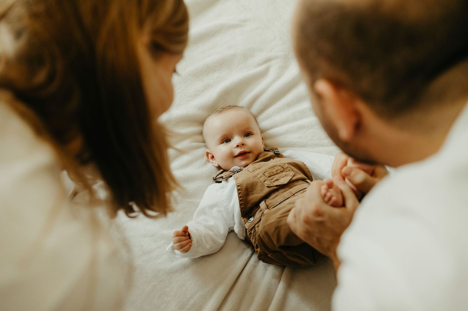 Bébé qui sourit à ses parents, allongé, regardant son papa, en tenue marron à Rodez en Aveyron