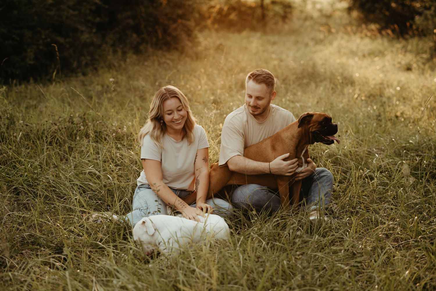 Couple souriant assis dans l'herbe avec leurs chiens Boxer à Saint Sulpice