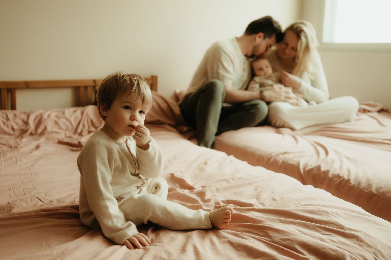 Séance photo lifestyle bébé, le grand frère habillé en beige regarde l'objectif pendant que les parents câlinent le bébé à Gaillac