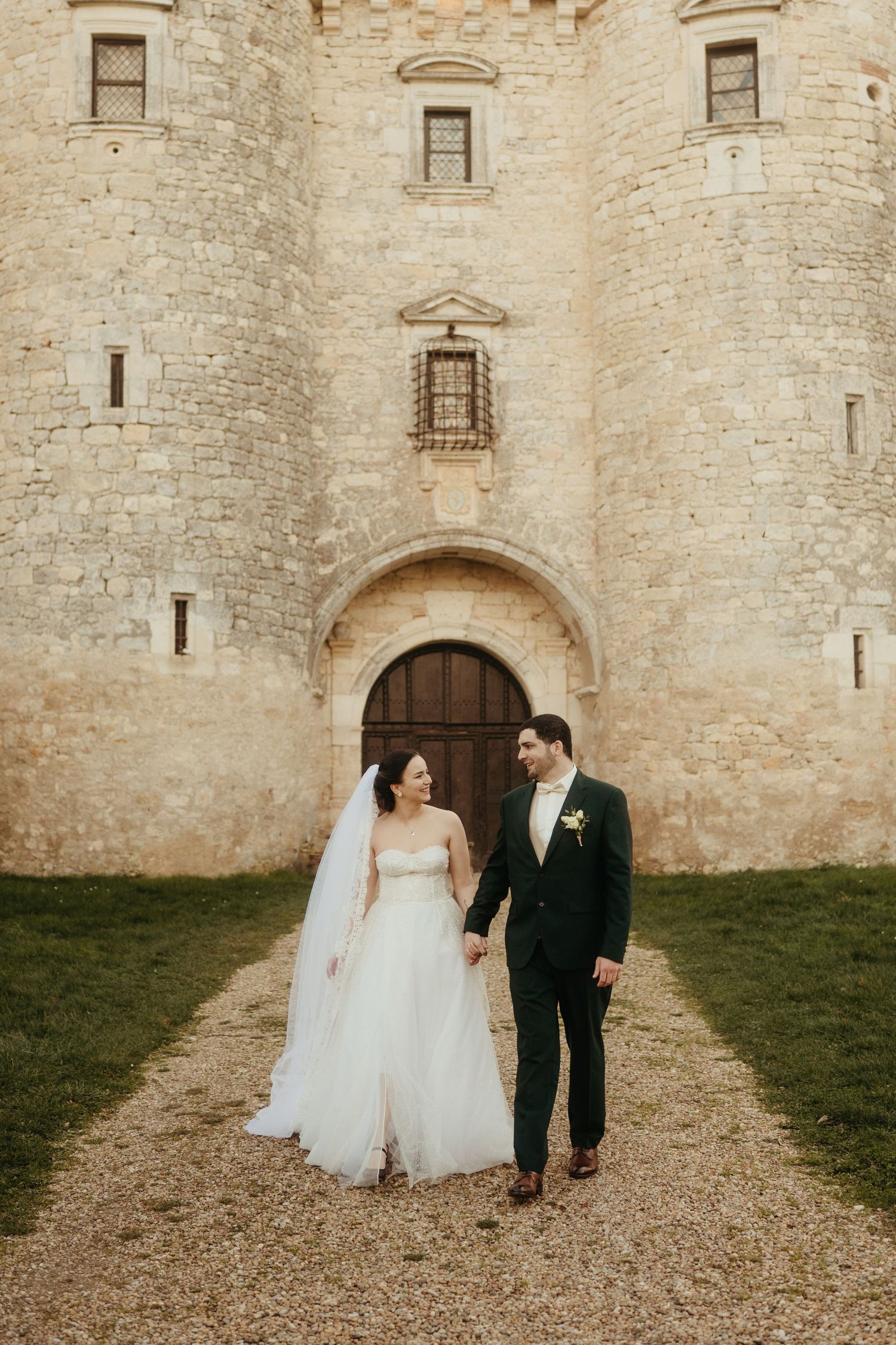 Mariée avec un voile en broderie marchant avec son mari devant le Château de Mauriac dans le Tarn