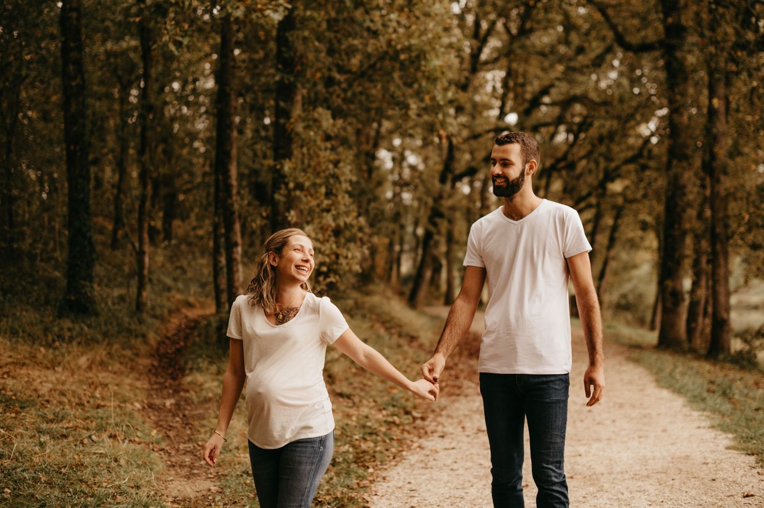 Un couple se promène main dans la main sur un sentier forestier lors d'une séance photo maternité automnale.