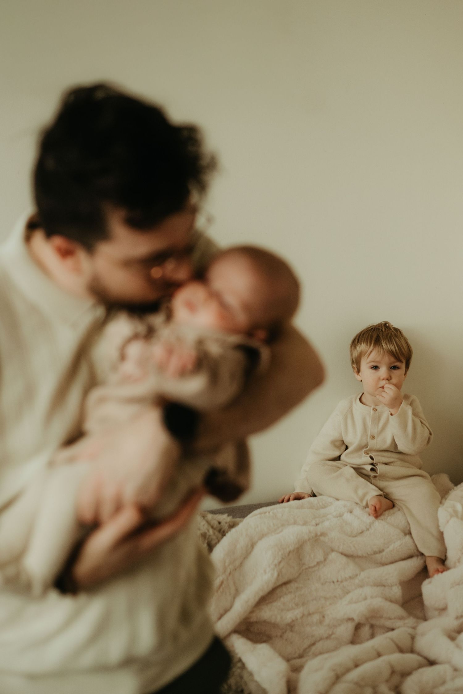 Séance photo de naissance, le papa embrasse son bébé de deux mois, sous le regard tendre de leur plus grand enfant