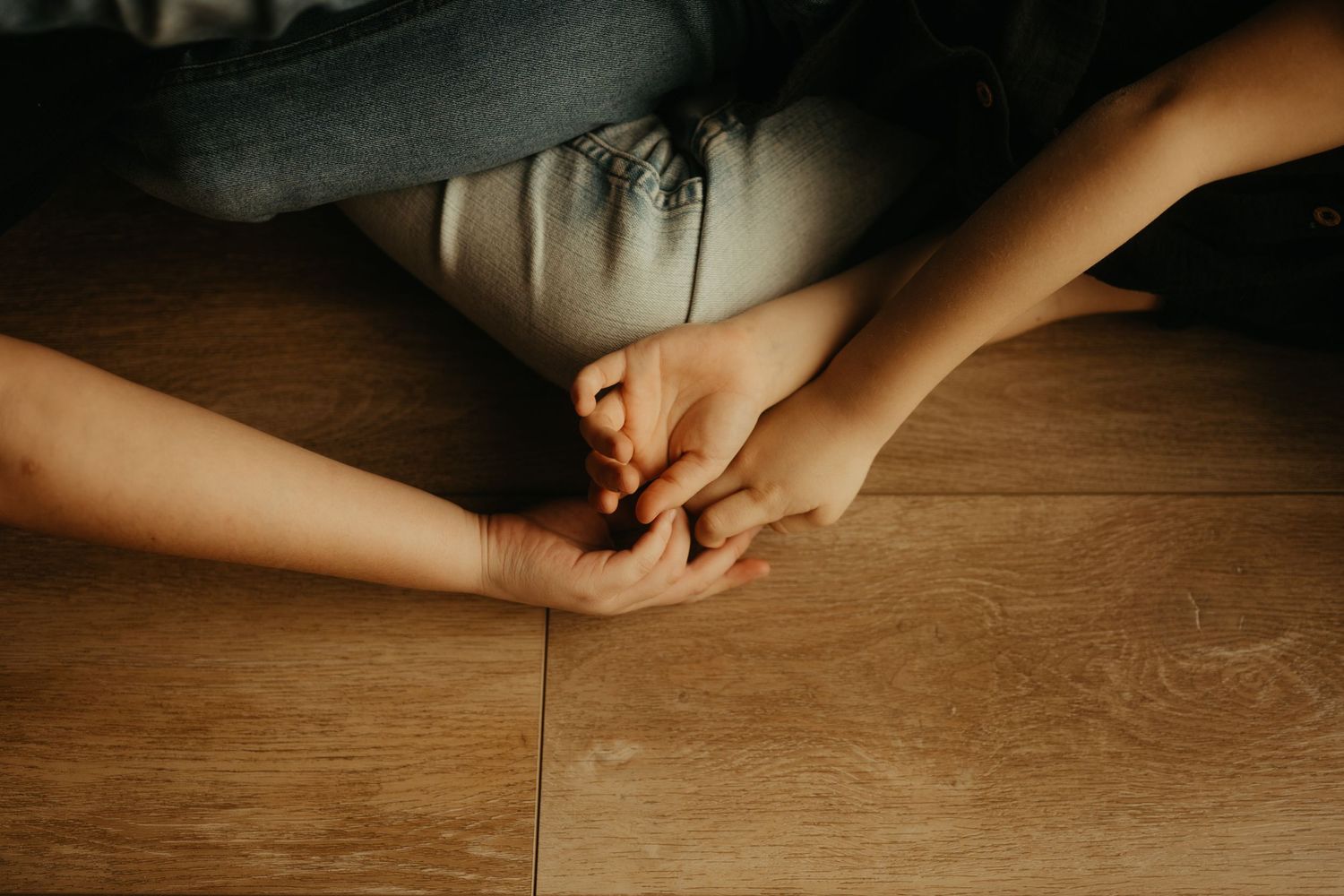 Détails de mains d'enfants, sur un parquet aux couleurs chaudes, pendant une séance photo de famille à domicile à Saint Sulpice la Pointe