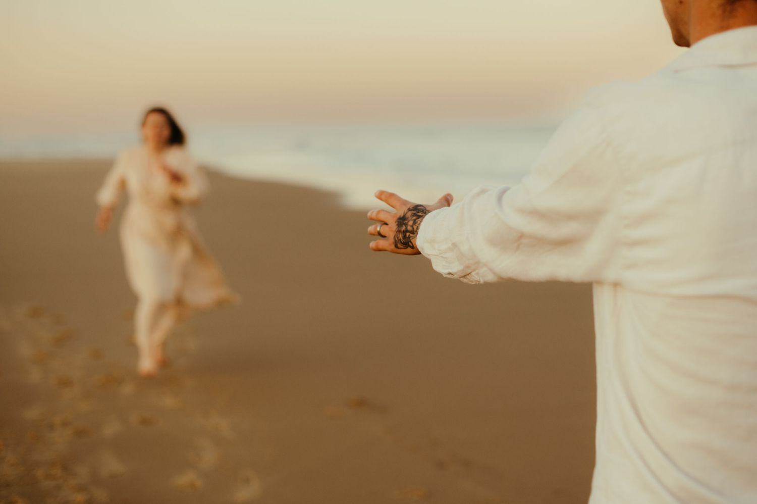 Séance couple , la main tatouée tendu vers la fille en robe beige qui vient en courant sur la plage à Labenne Océan