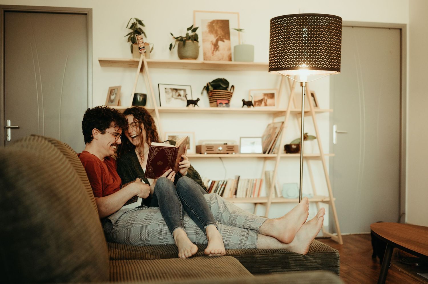 Couple sur leur canapé, dans leur salon, lisant un livre en riant à Carmaux