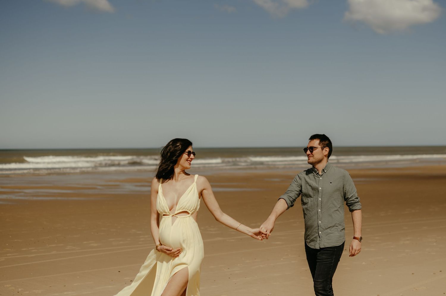 Futurs parents en séance maternité sur la plage, marchant sur le sable, l'océan au loin à Lacanau