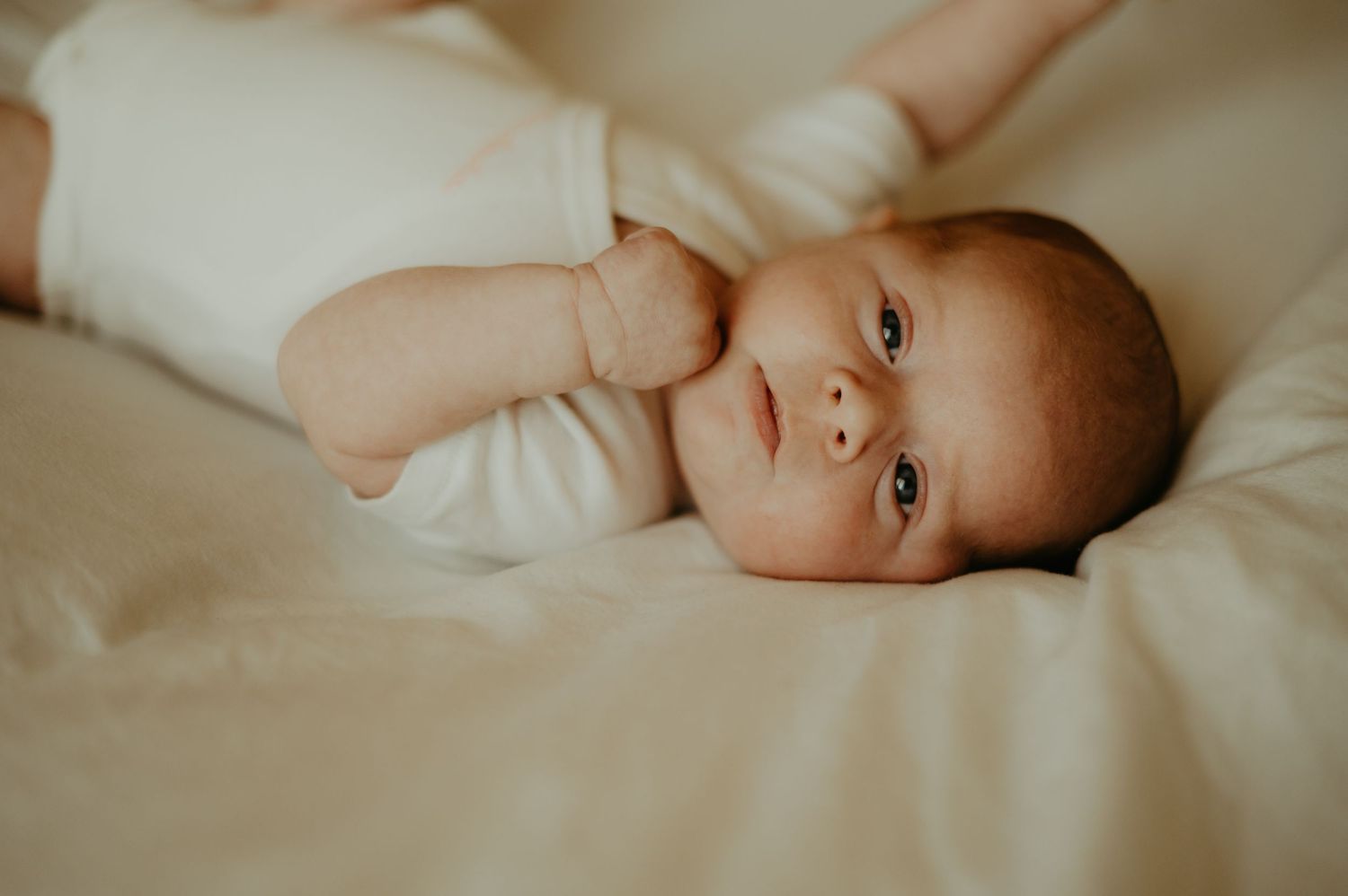 Séance naissance, un bébé regarde l'appareil photo en étant sur un drap blanc, à Saint Sulpice la Pointe