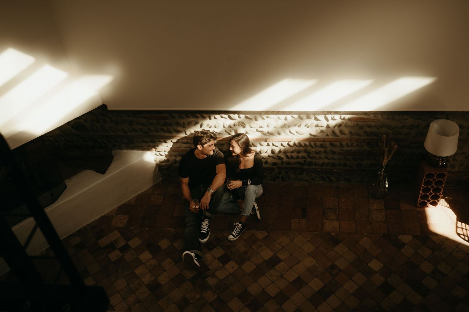 Portrait de couple, assis dans leur salon, contre un mur de pierres à Toulouse