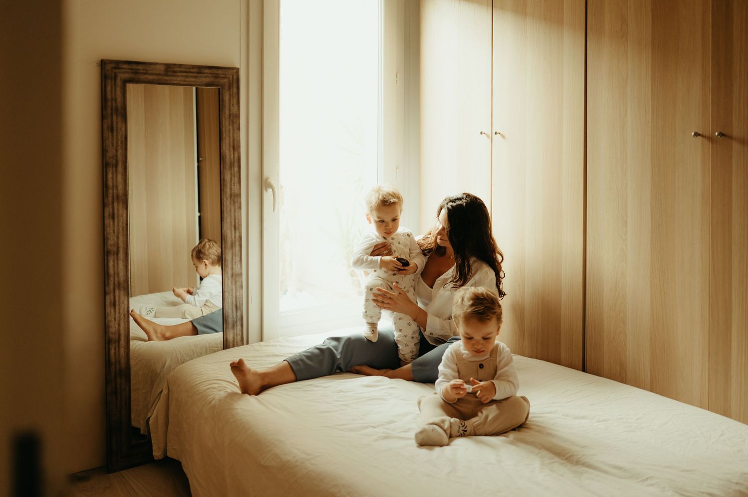 Maman jouant avec ses deux enfants jumeaux sur le lit, dans une lumière douce et naturelle, à domicile à Toulouse