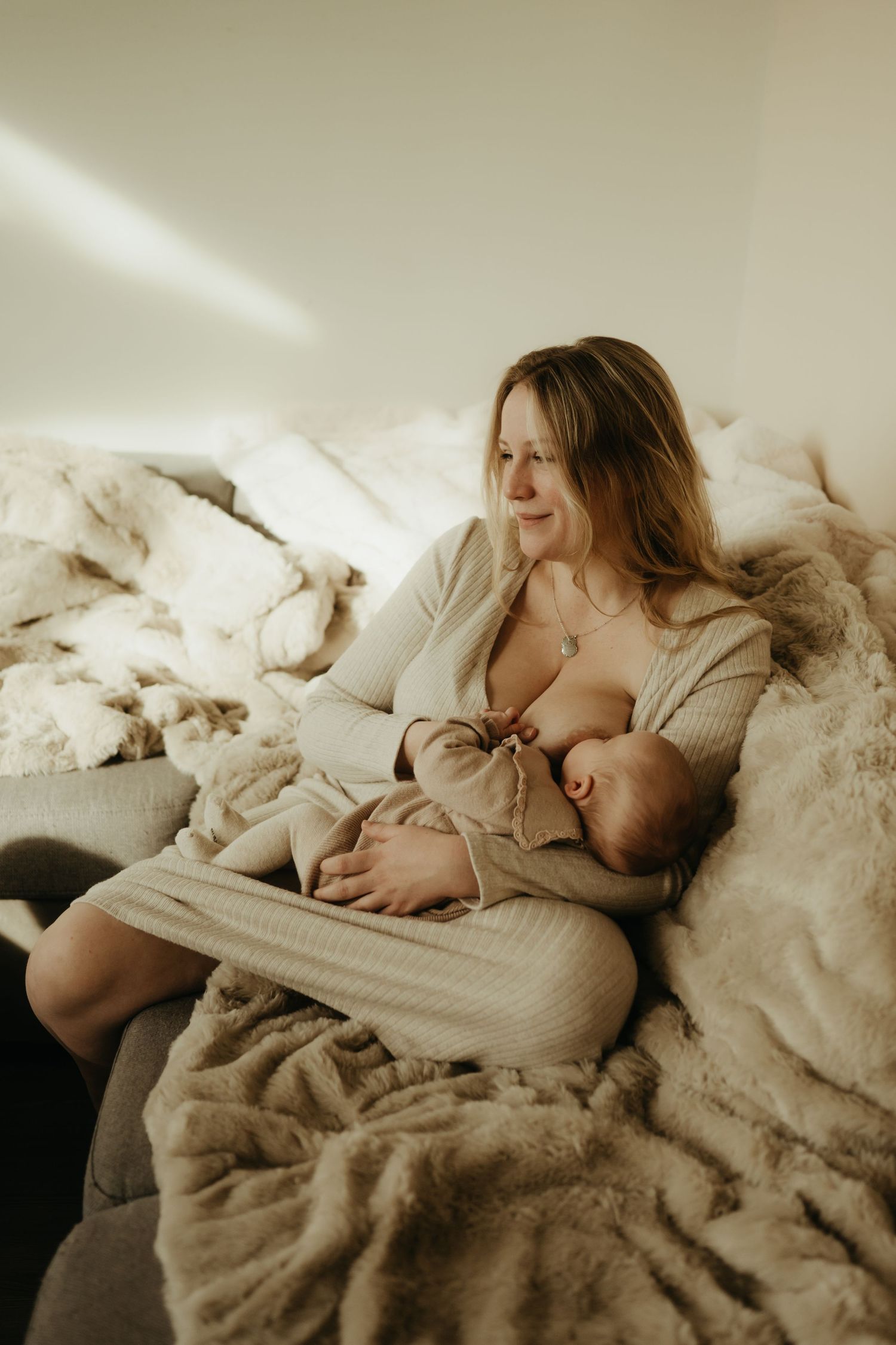 Séance naissance, maman habillée en beige allaitant son bébé sur le canapé à Gaillac