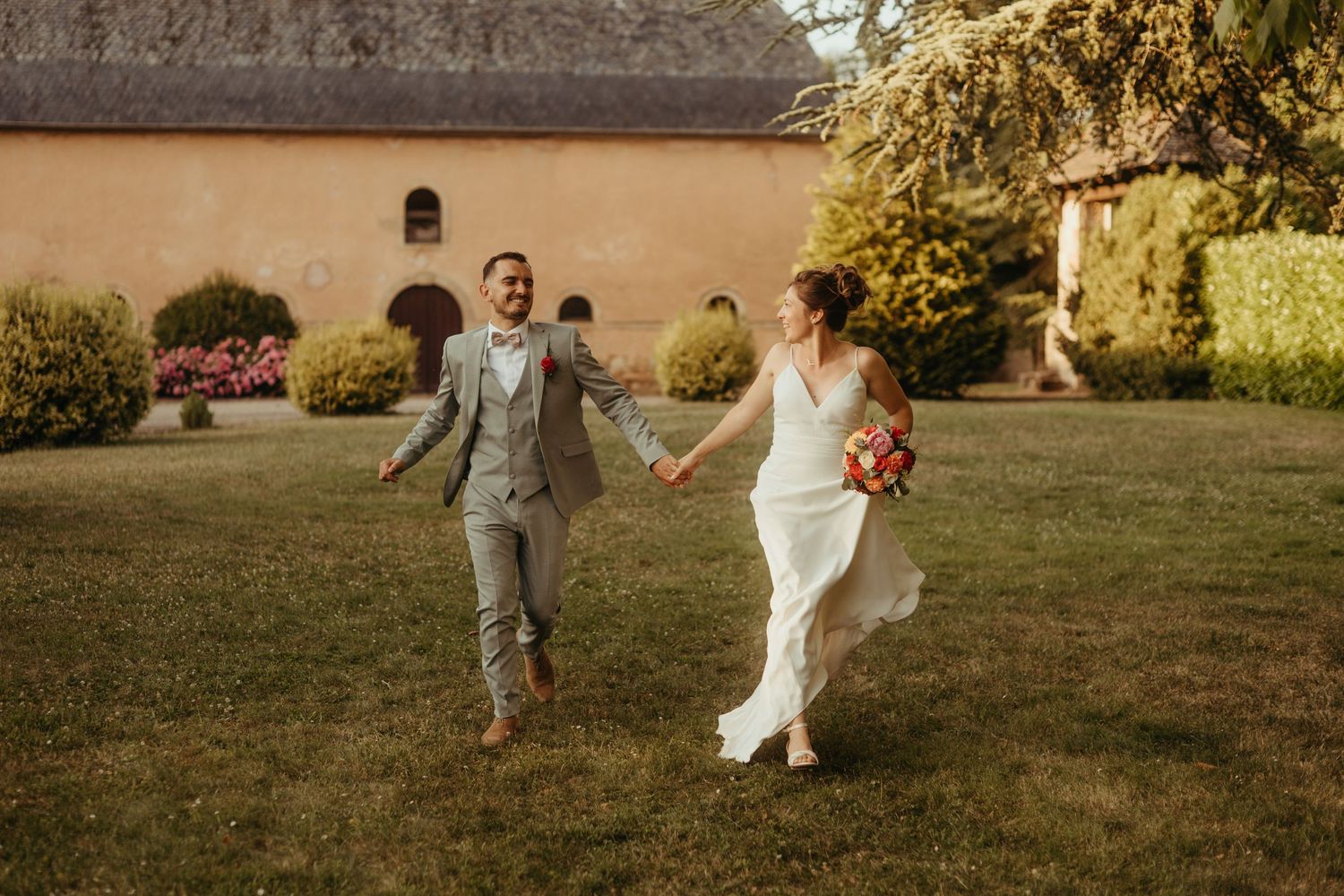 Couple de jeunes mariés, qui courent en riant, pendant leur séance photo de couple au Domaine de la Goudalie, en Aveyron