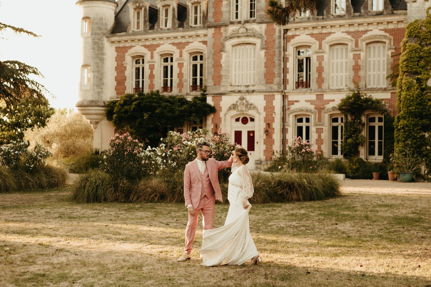 Mariés dansant devant un château en Charente, la robe tournoyant, au couché du soleil