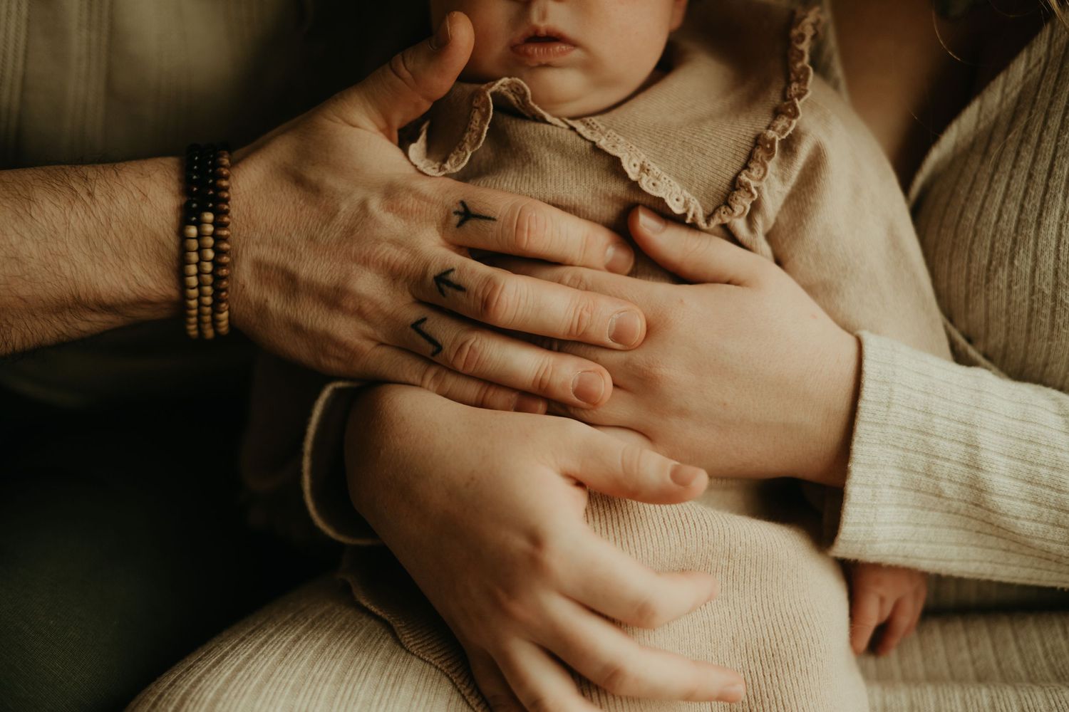 Séance de bébé, tenu par ses parents, d'une main tatouée, dans une tenue beige près d'Albi