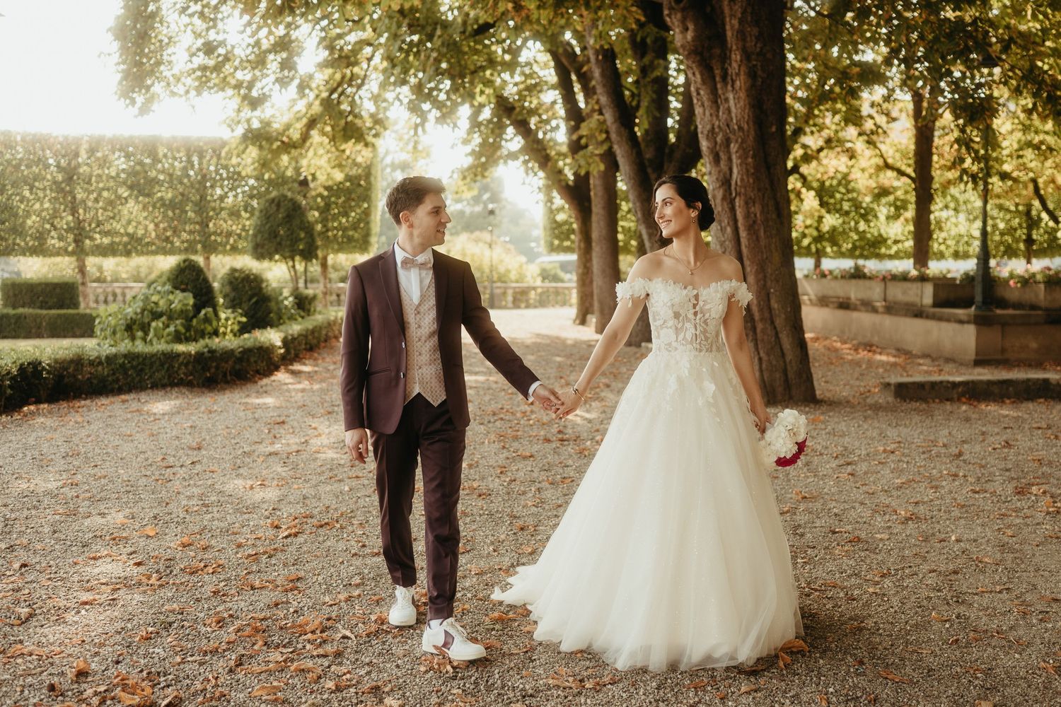 Marié au costume bordeaux, tenant la main de la mariée à la jolie robe dans le parc de la mairie de Castres, un matin d'août