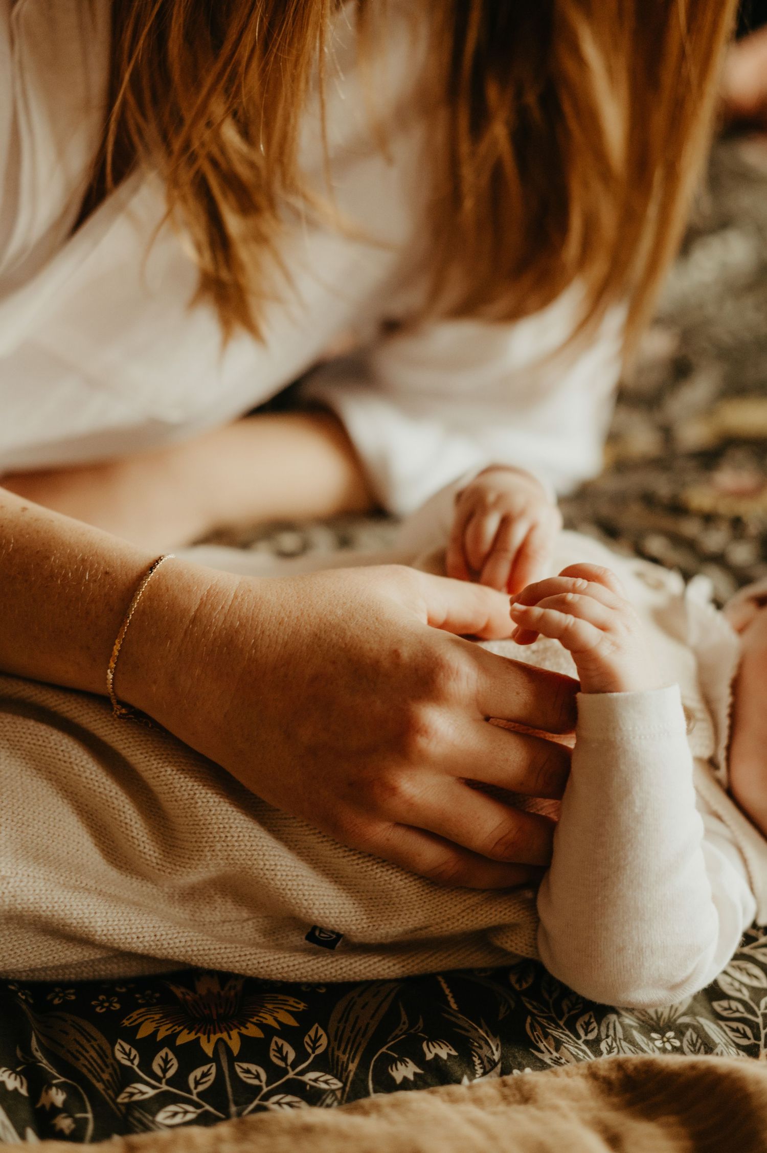 Détail de main de maman qui tient son bébé en tenue beige, posé sur le lit à Saint Sulpice