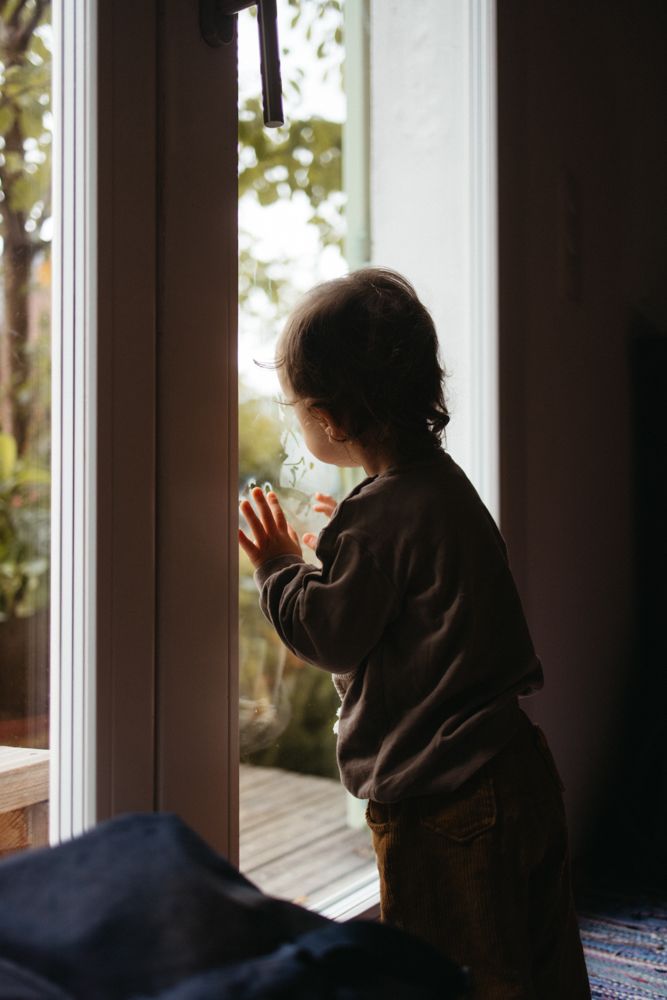 Junge schaut bei einem dokumentarischen Familienshooting aus dem Fenster