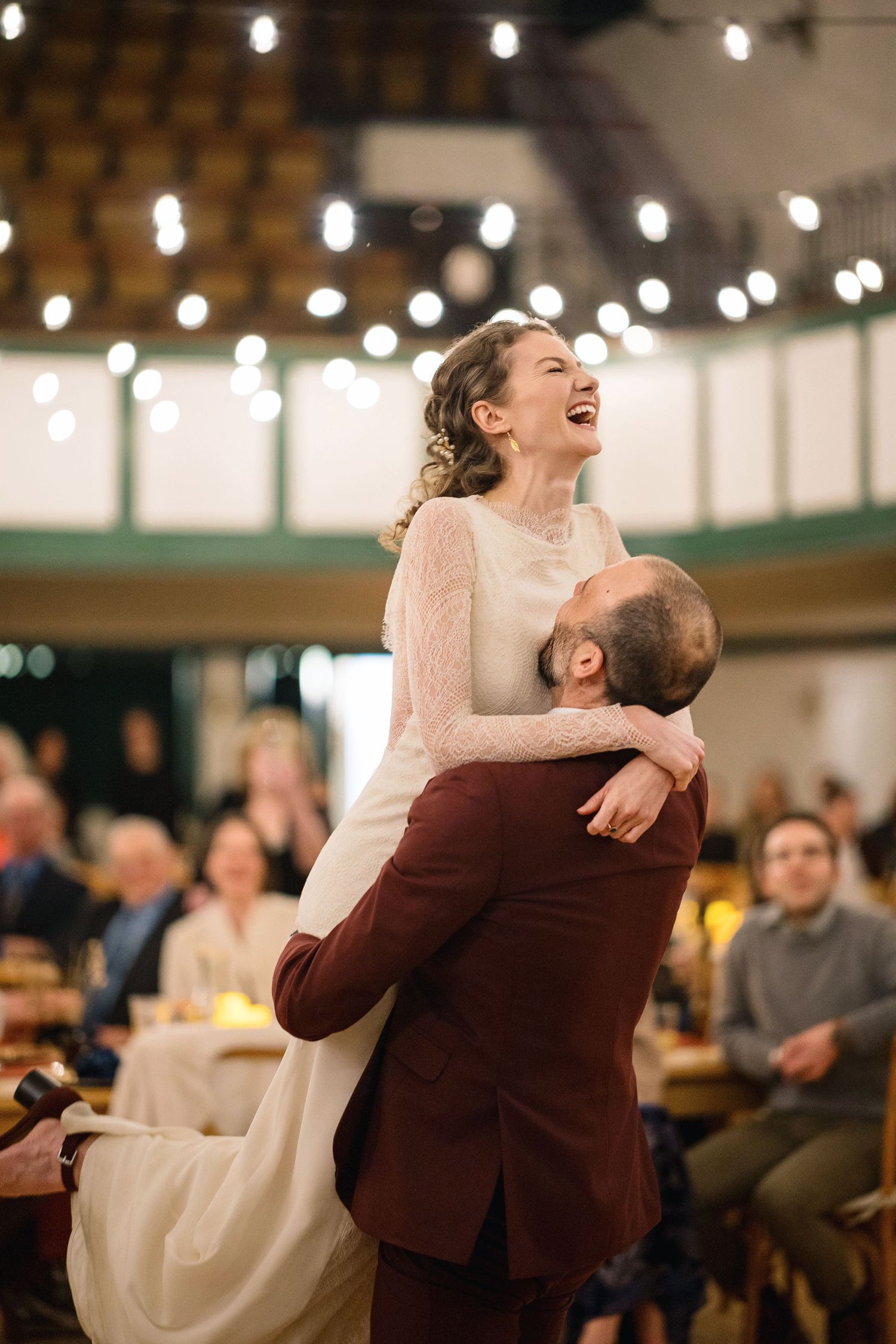 A couple shares a joyful dance moment at an indoor reception venue decorated with string lights.