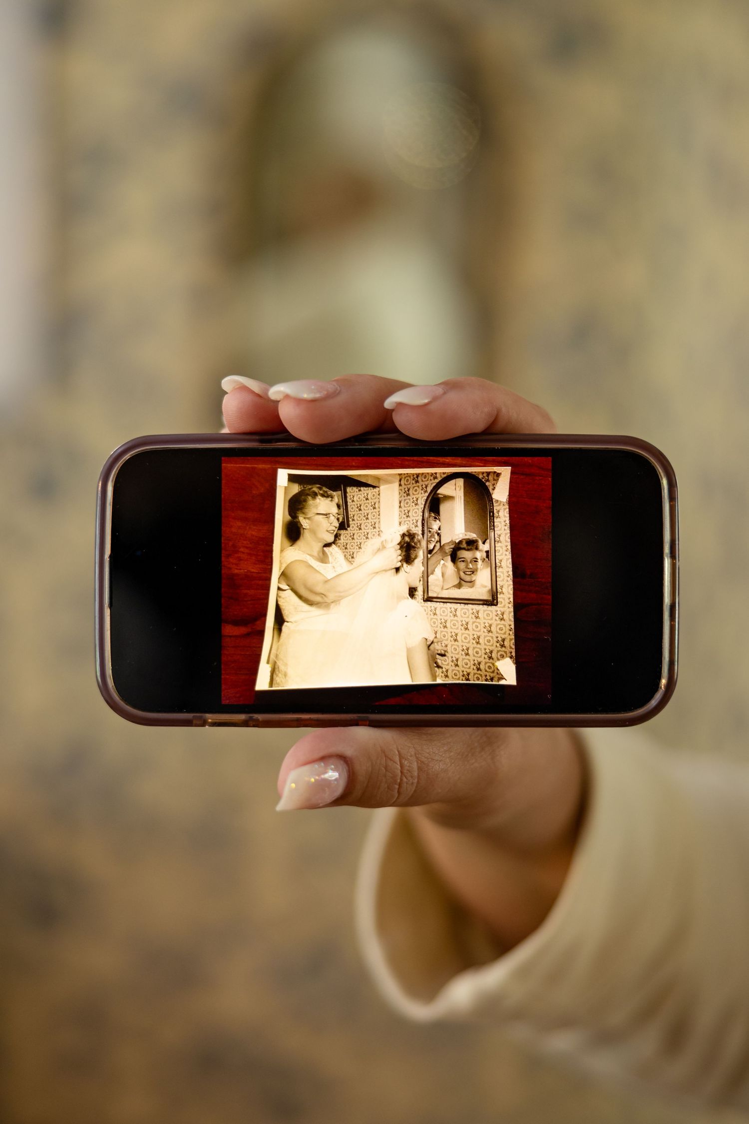 Hand holding smartphone displaying vintage black and white photo of woman at vanity mirror, retro 1950s style.