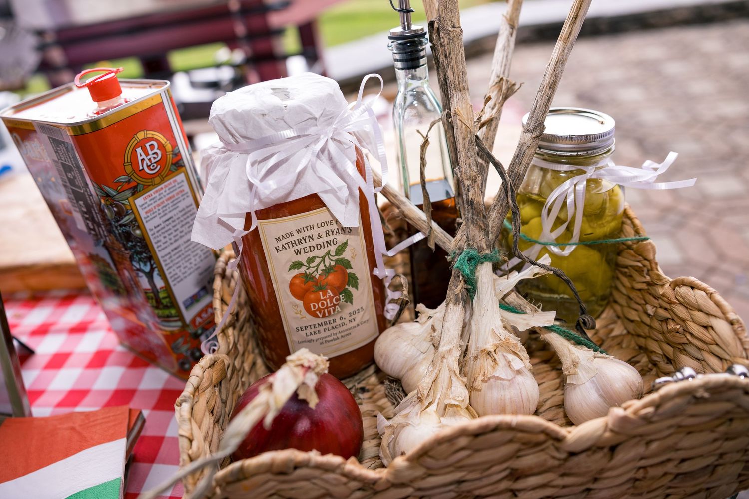 Wicker gift basket filled with tomato sauce, olive oil, garlic, and gourmet Italian ingredients on a checkered tablecloth.