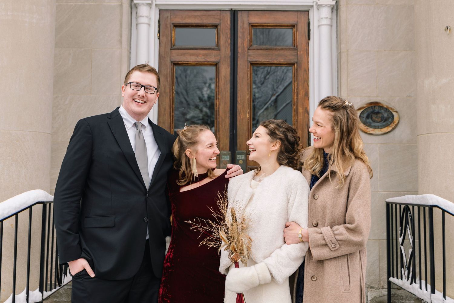 A couple shares a joyful moment together while standing outside elegant wooden doors.