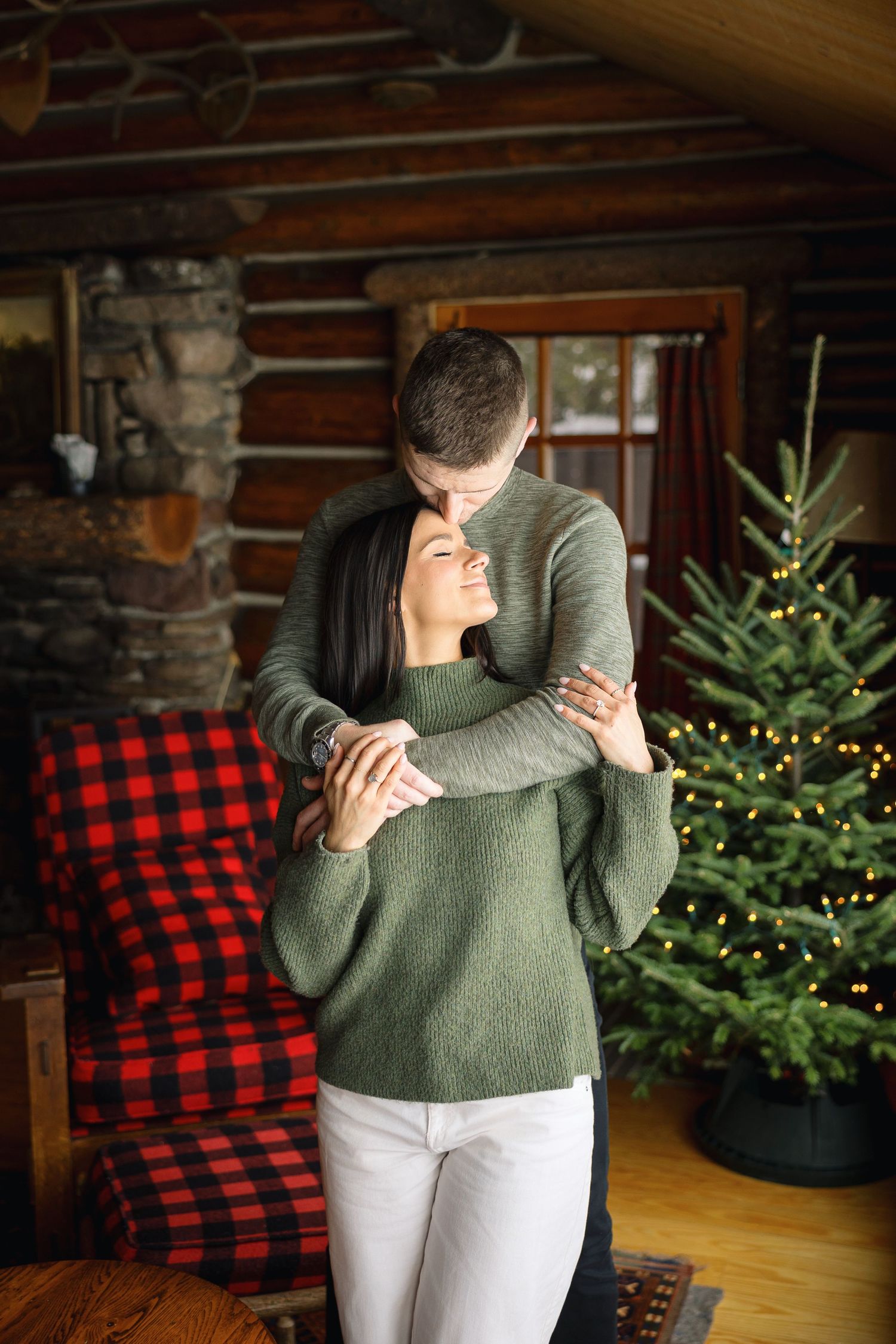 A cozy winter embrace in a rustic cabin with a Christmas tree in the background.