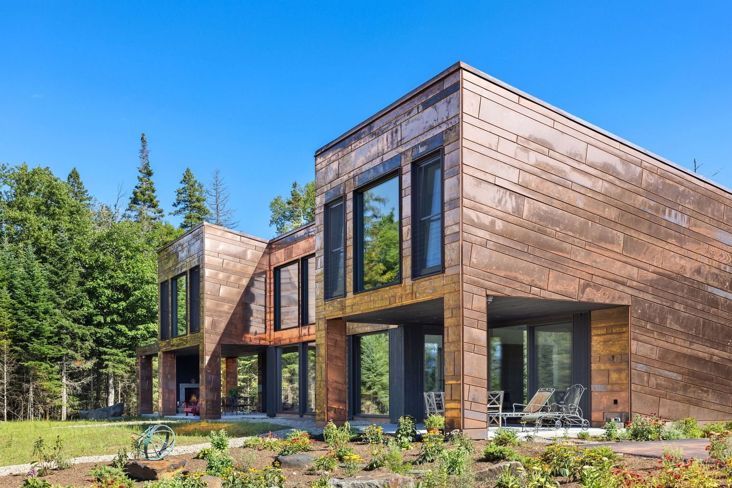 Modern wooden cabin with large glass windows nestled in a scenic forest setting with blue sky overhead.