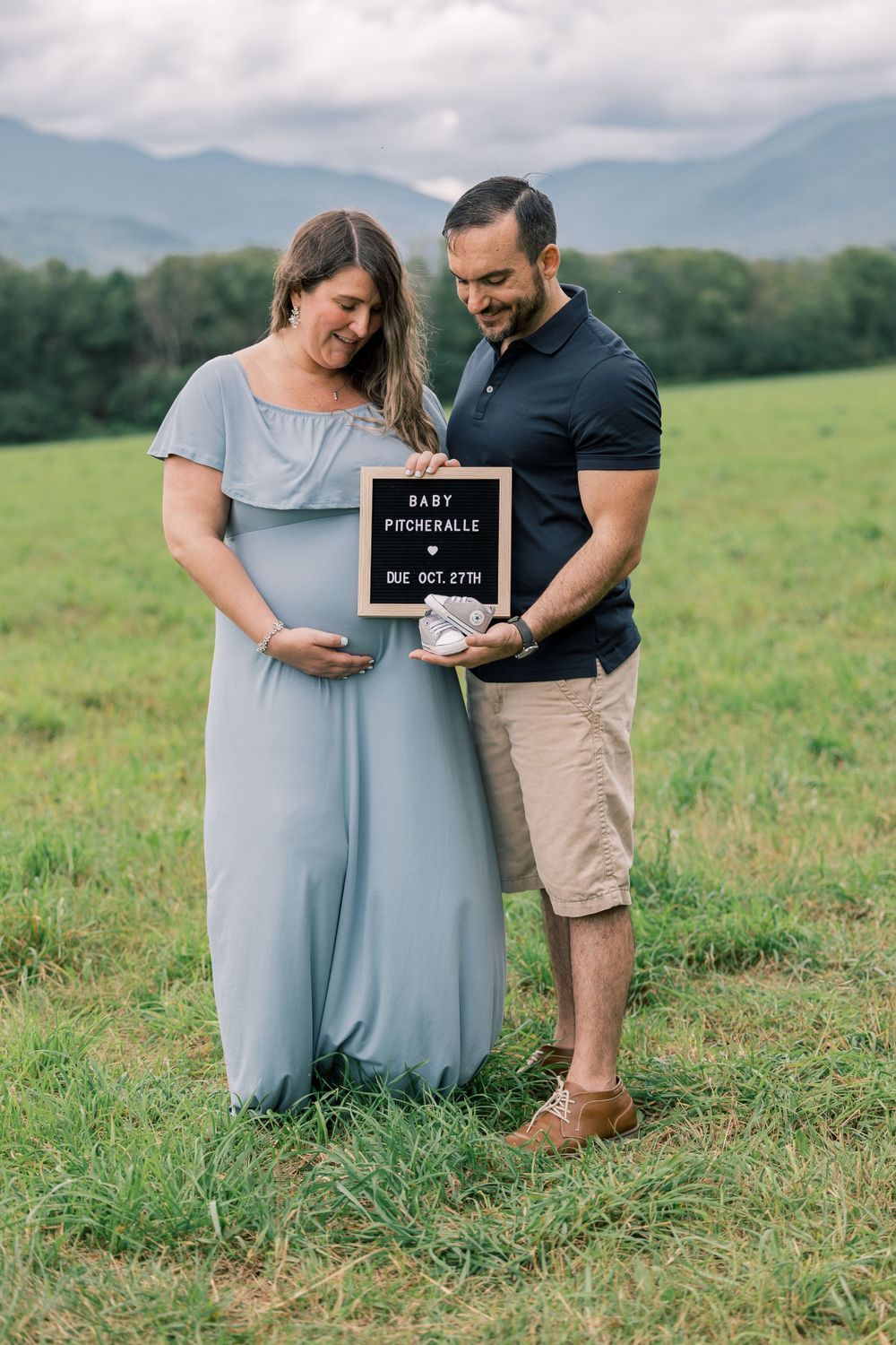 A couple in a grassy field shares a tender moment during their pregnancy announcement photoshoot.