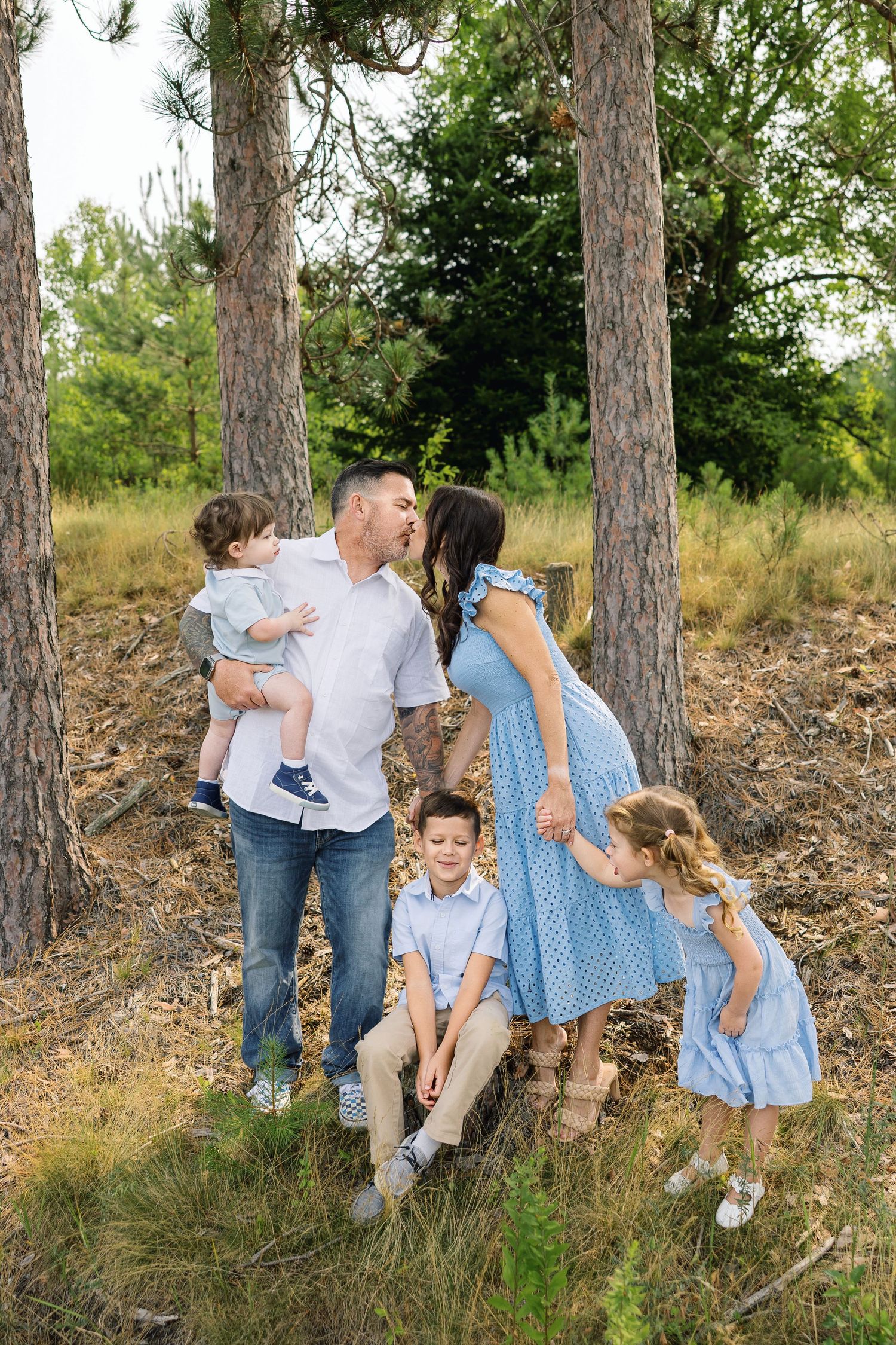 A group in coordinated blue and white outfits shares candid moments together among tall pine trees in a natural setting.