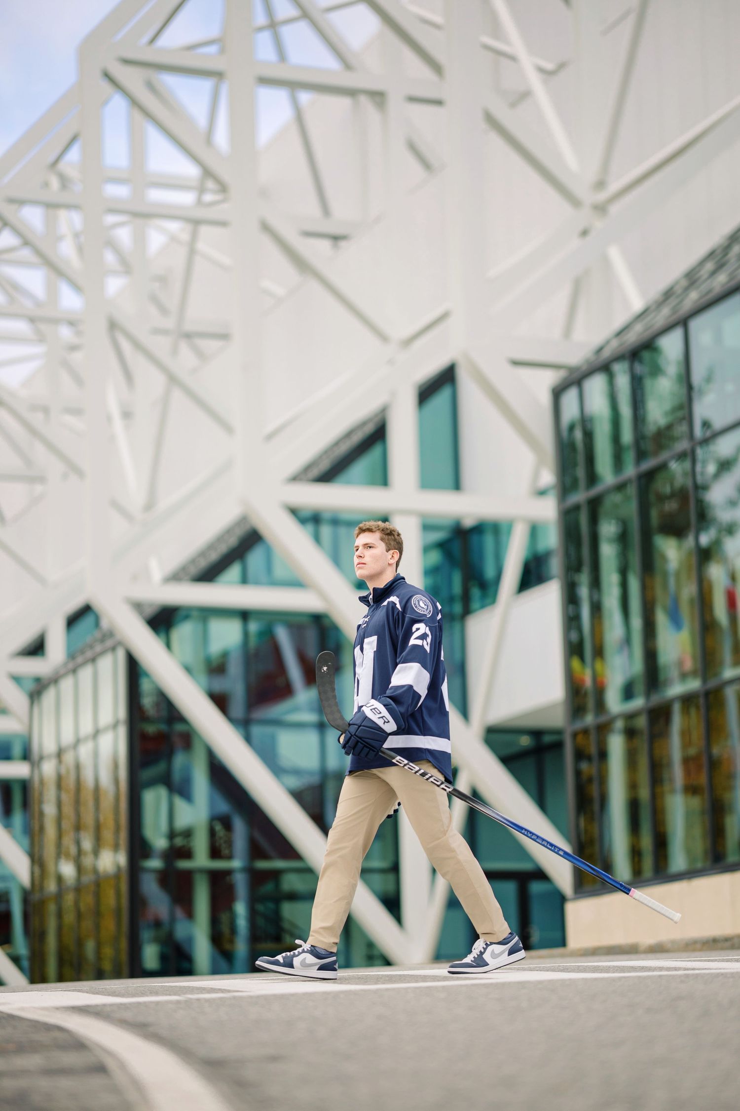 Person in navy jacket and khaki pants sits on modern architectural structure with geometric white patterns and glass walls.