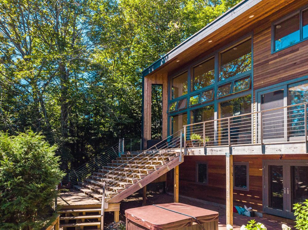 Modern wooden deck with glass railings connects multiple levels of a contemporary home surrounded by lush greenery.