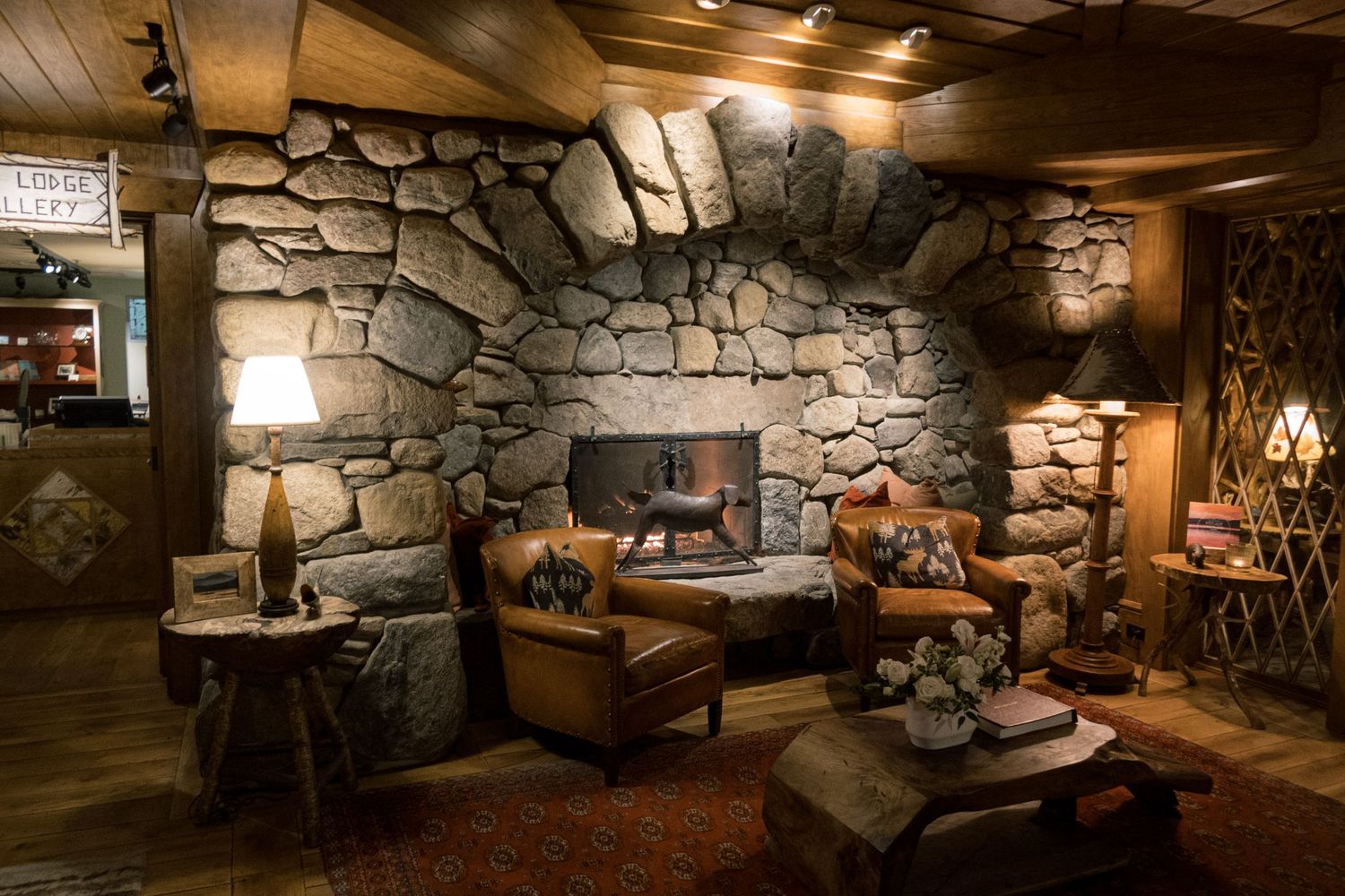Rustic stone fireplace with leather armchairs in a cozy lodge-style living room with warm ambient lighting.