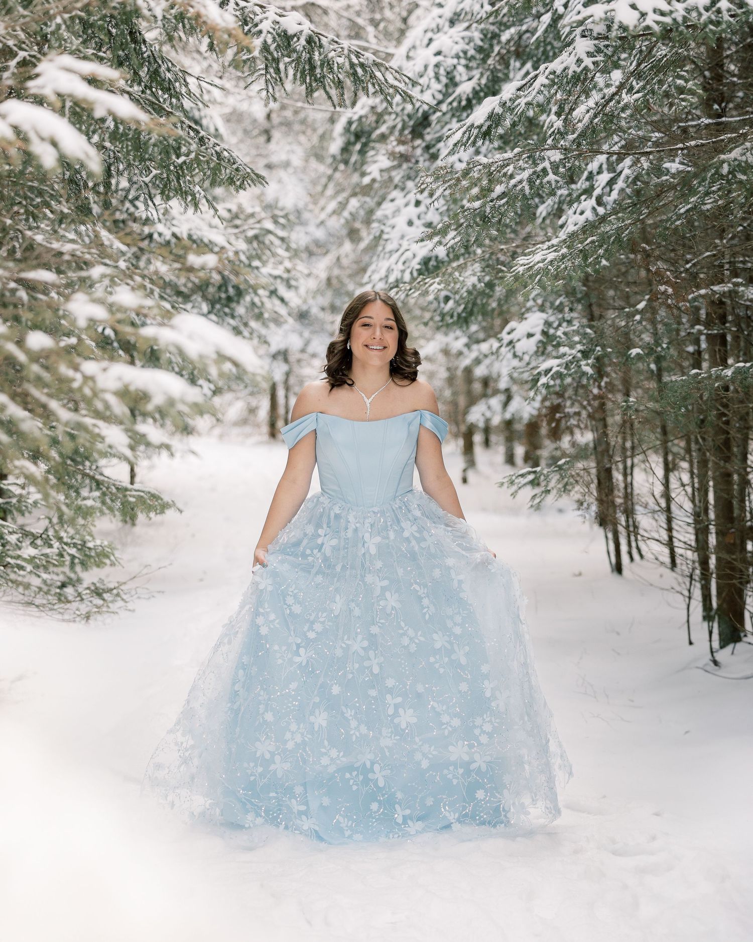 A light blue ballgown dress twirls gracefully in a snow-covered forest setting creating a magical winter scene.