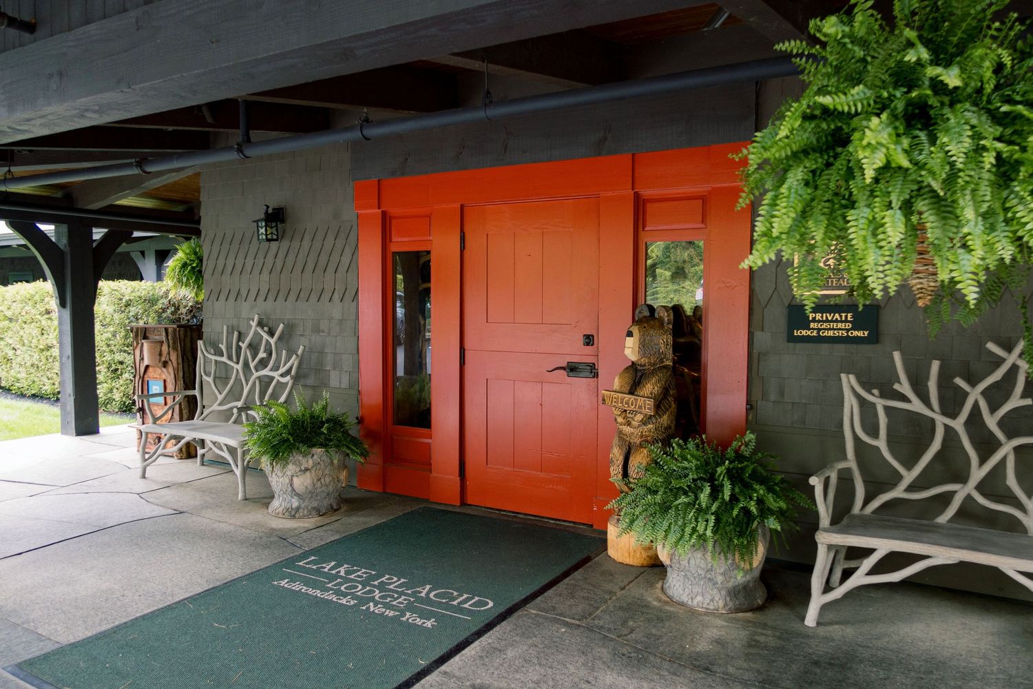 Elegant entrance of Lake Placid Lodge featuring a bold orange door, lush ferns, and decorative white bench.
