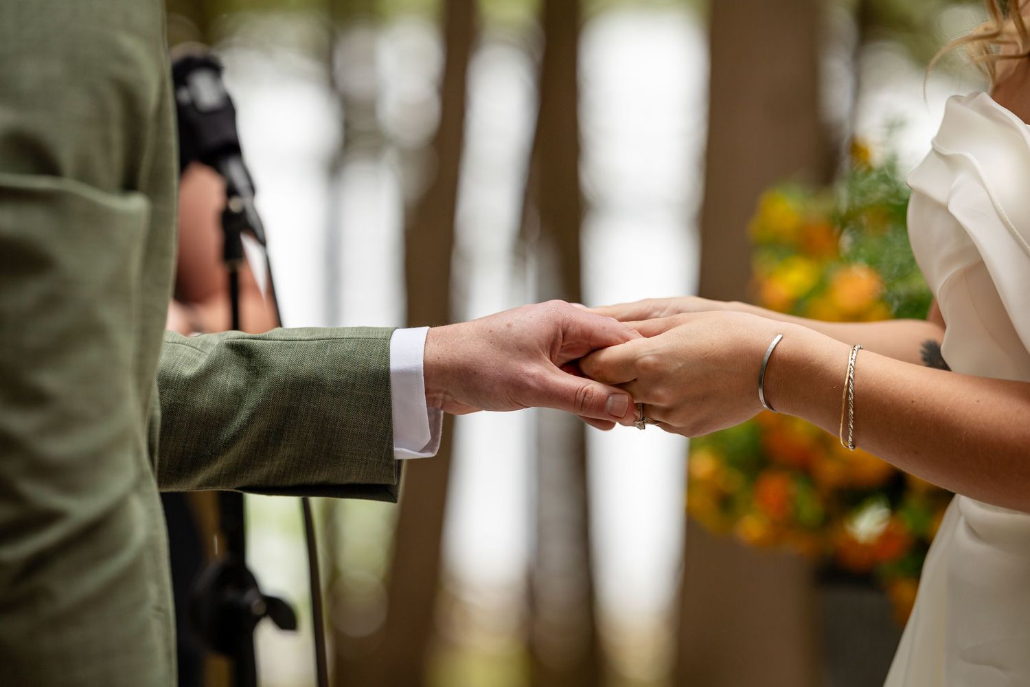 Bride and groom exchanging rings during outdoor wedding ceremony, close-up of hands with gold band.