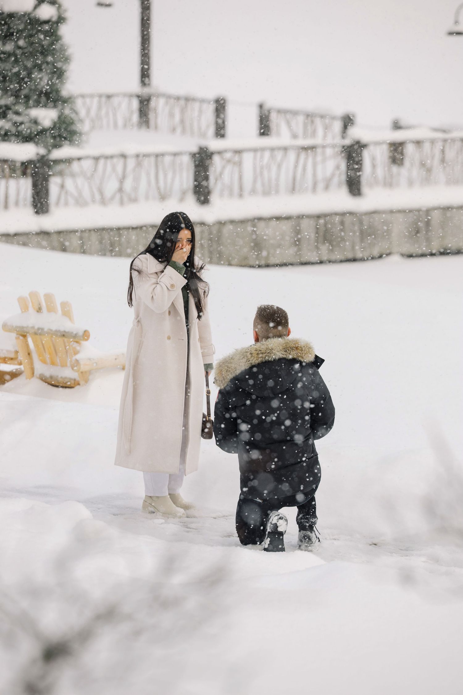 A romantic proposal scene in falling snow with a winter landscape backdrop.