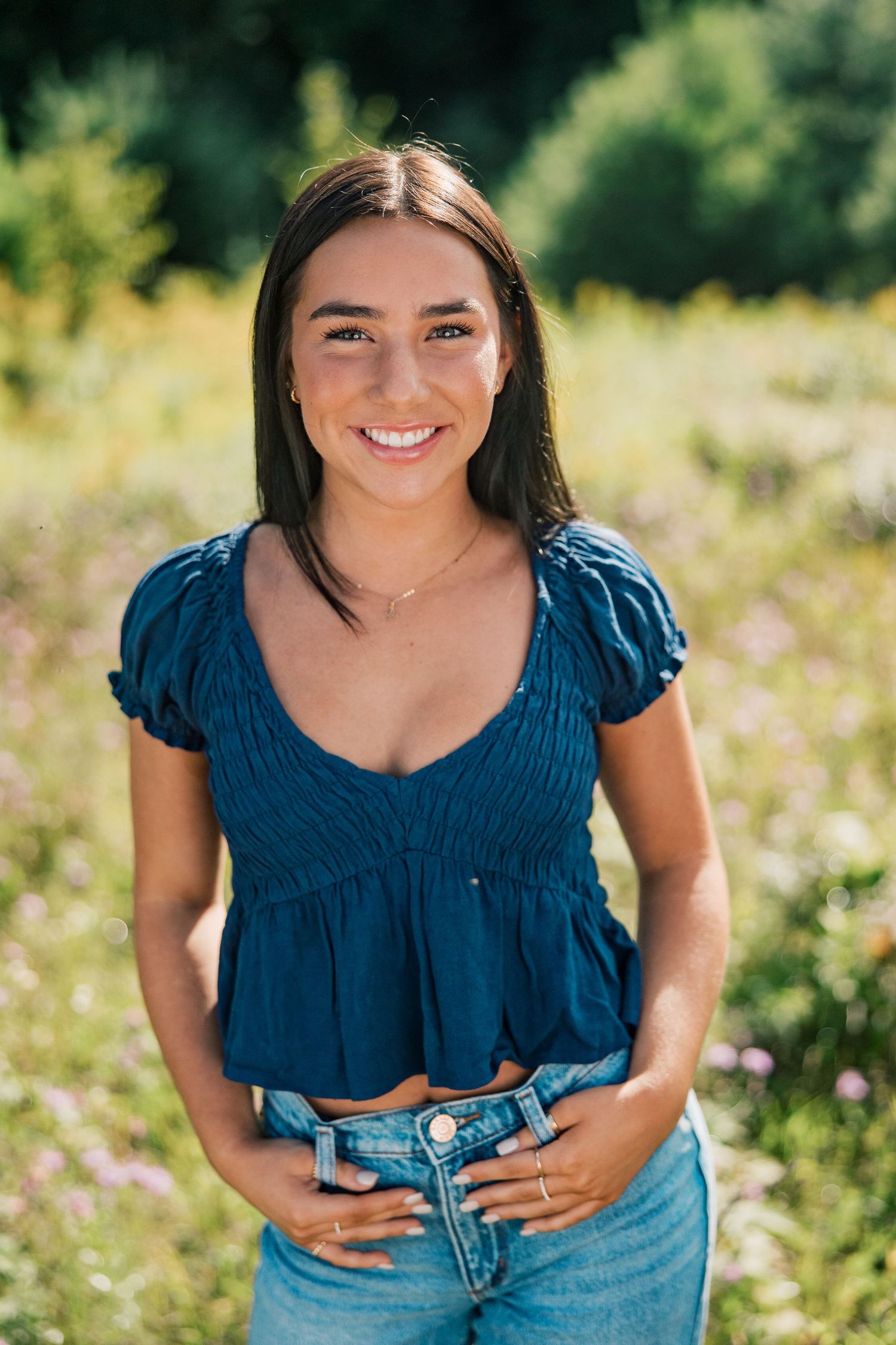 A series of four cropped photos showing someone in a navy blue top and denim jeans posing in a sunny wildflower field.